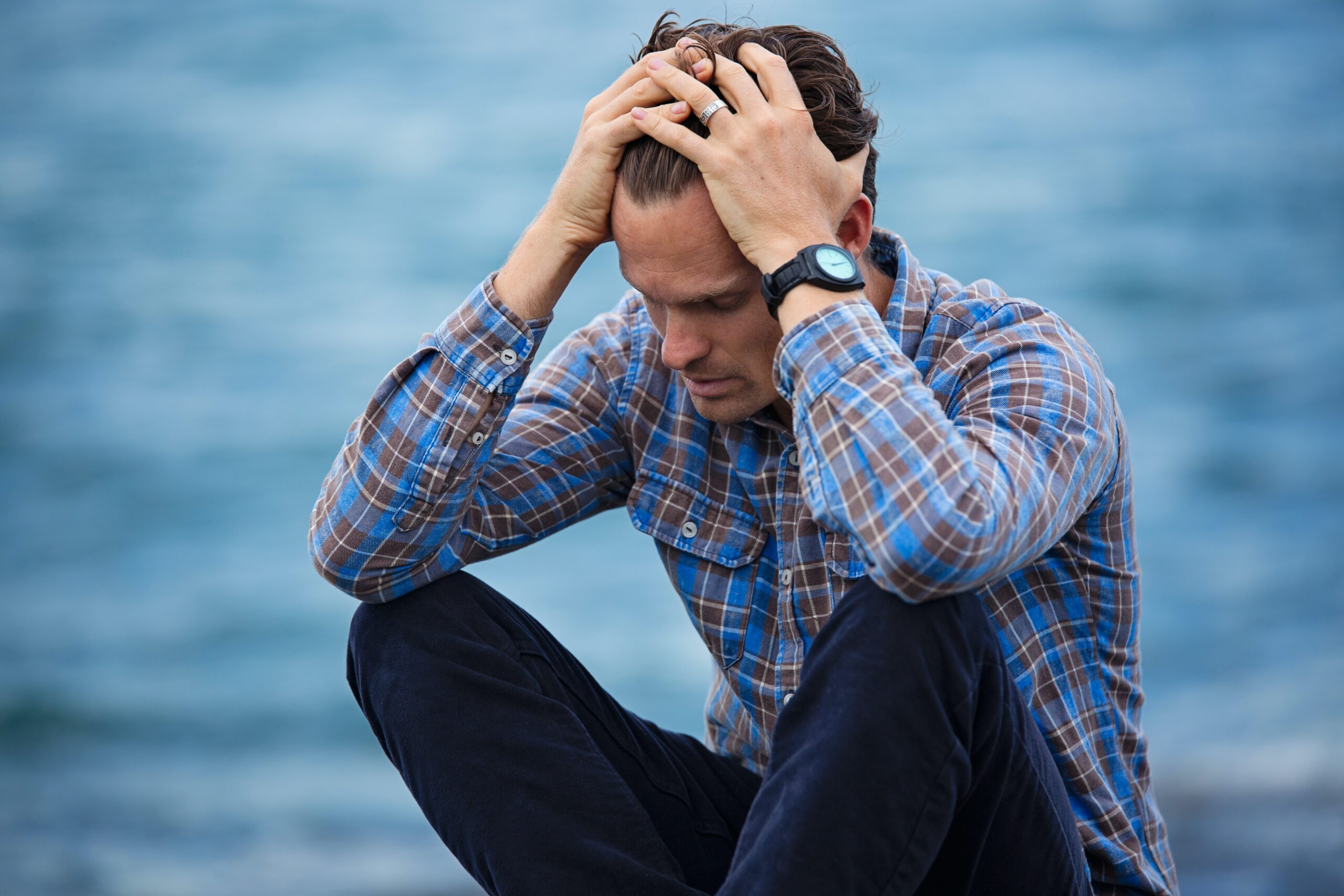 man sat by water with his head in his hands to depict living with fibromyalgia