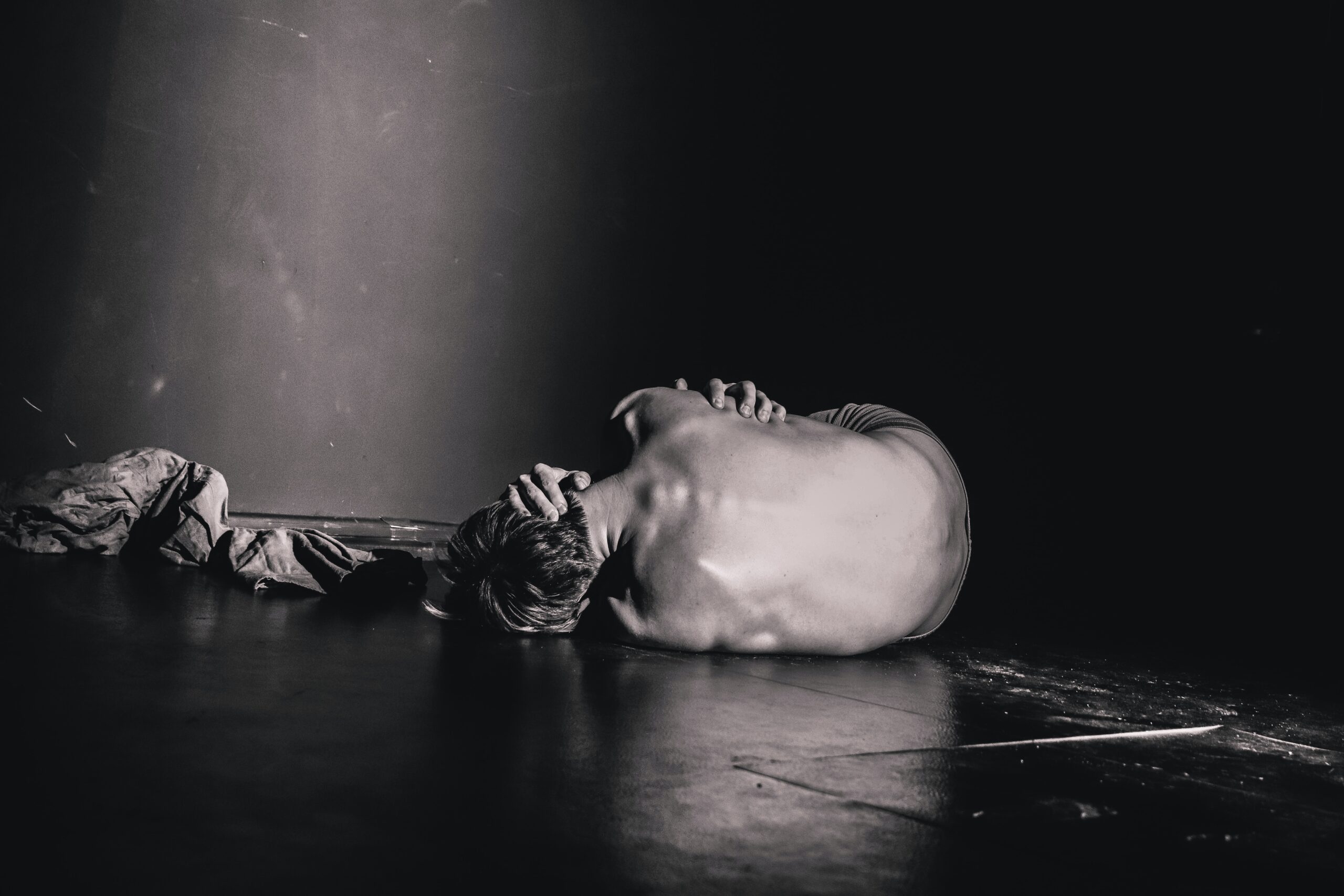 person lying on a floor head in hands in a grey scale image