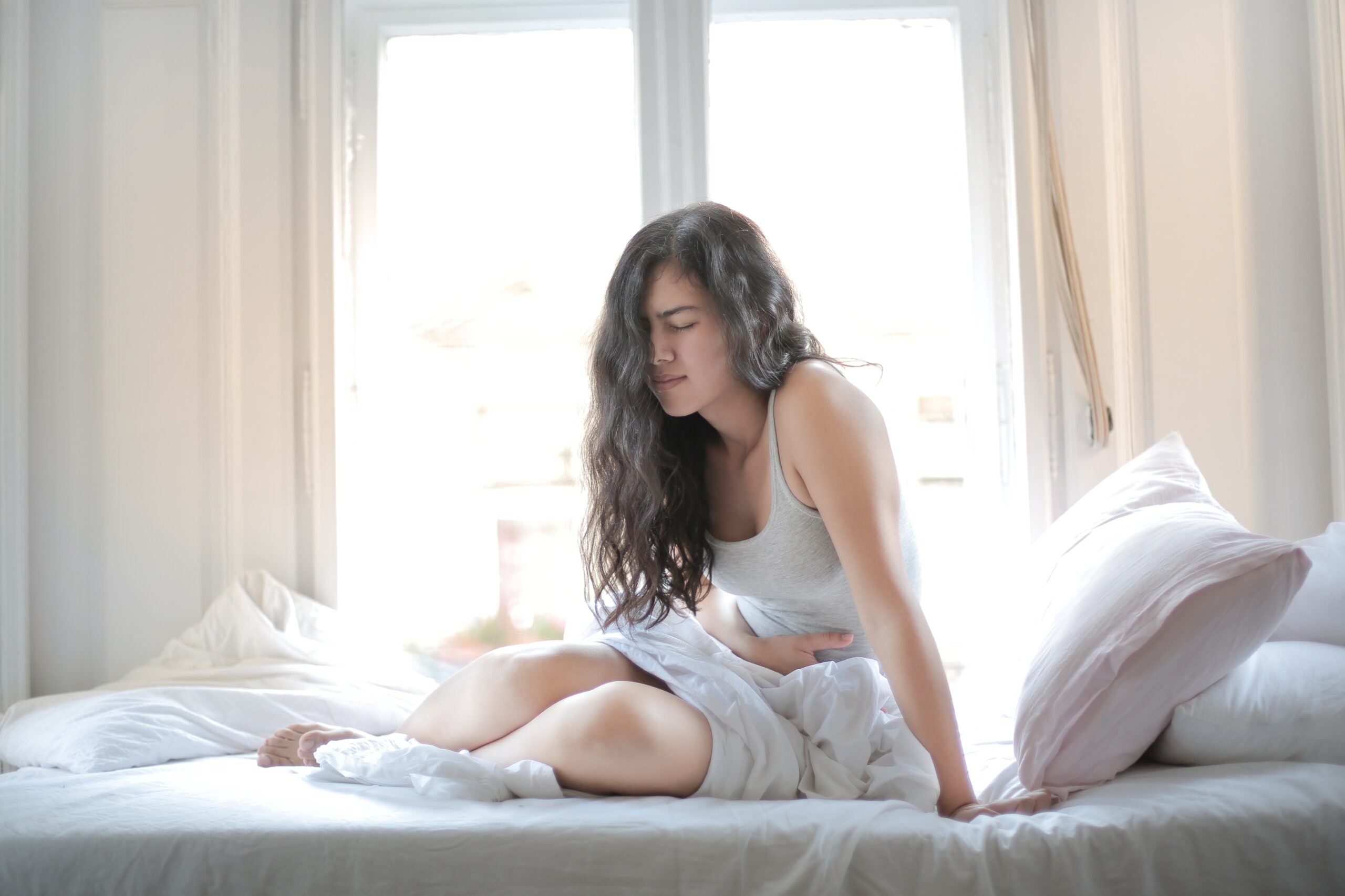 woman with dark hair lying on a bed in pain used in a blog for what causes fibromyalgia