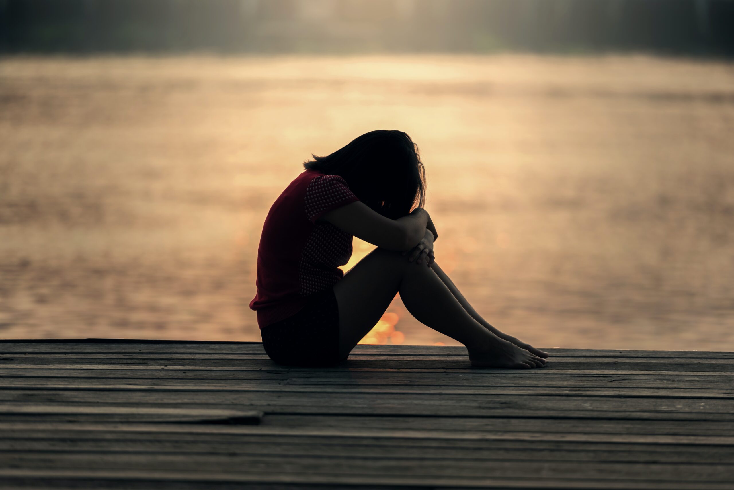 silhouette of a woman sitting with her head on her knees in front of water