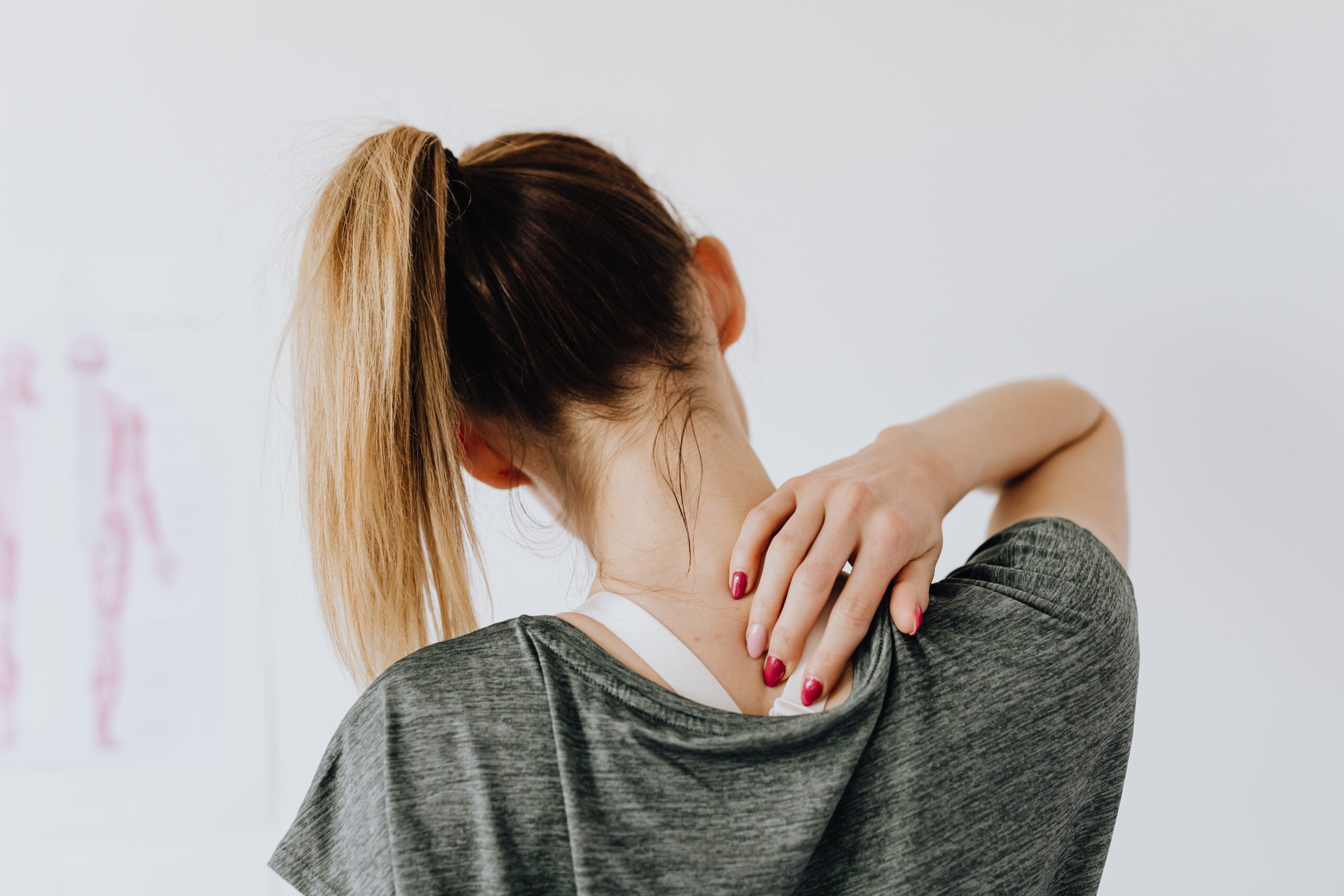 the back of a woman with her hand reached over to the back of her neck