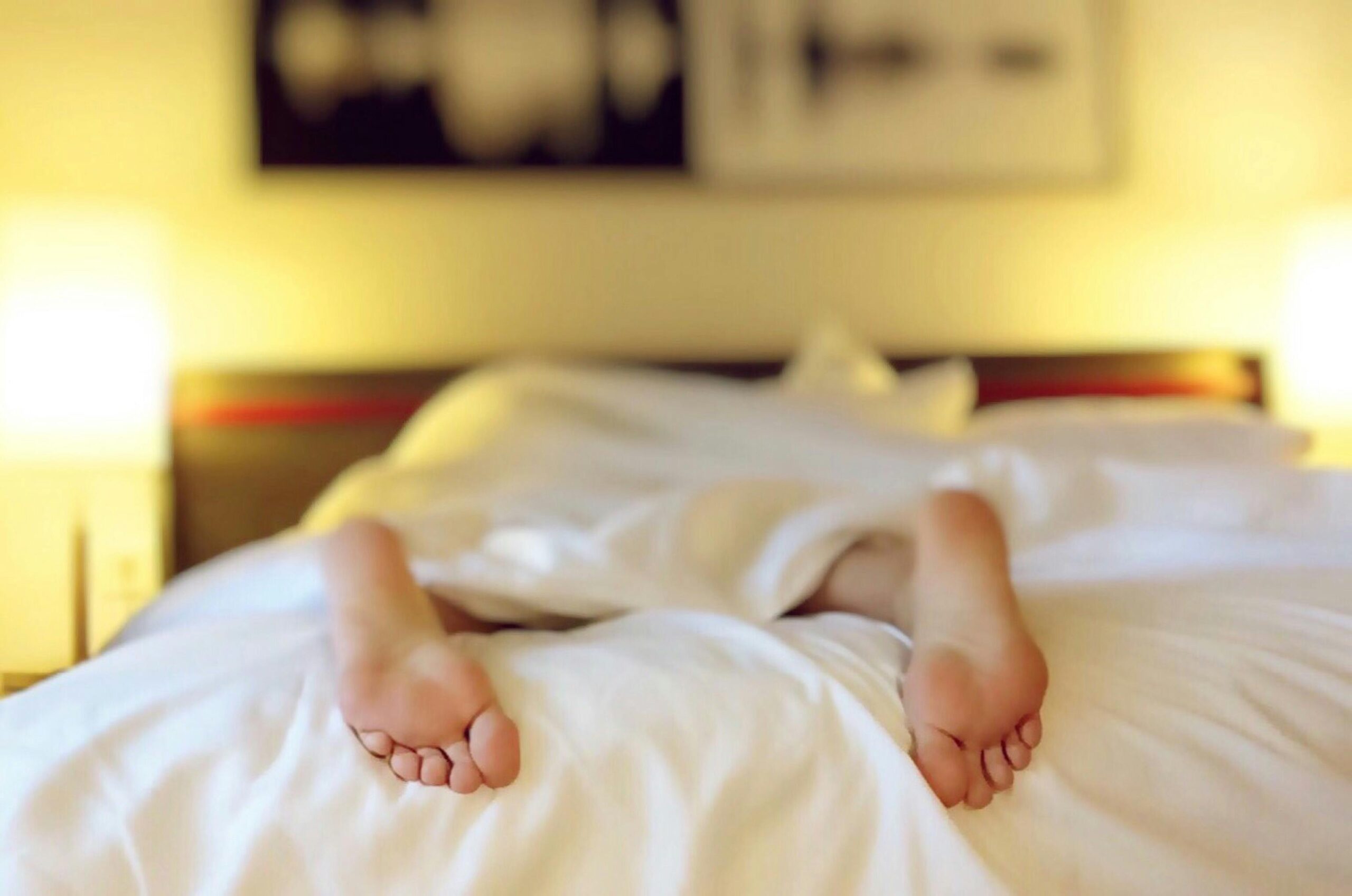 a shot of a perosn in bed feet facing the camera body under a white sheet