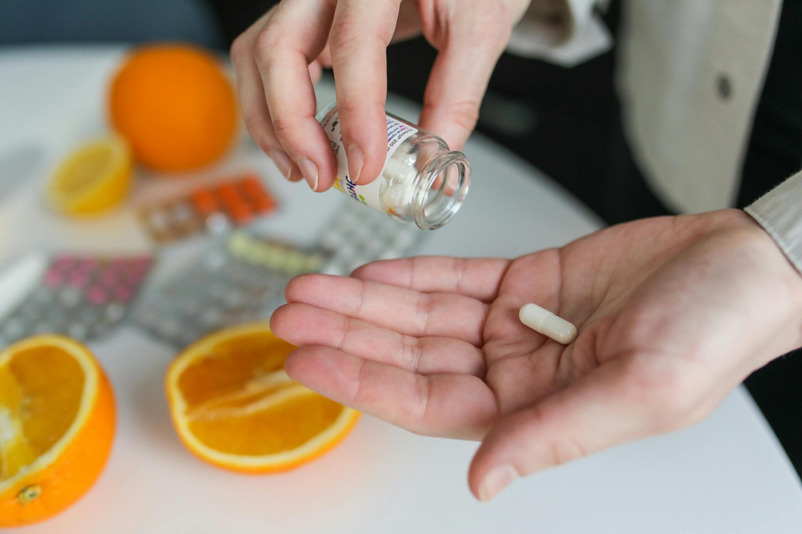 a single pill being tipped out of a small bottle into a persons hand with medicaiton under the hand on a table